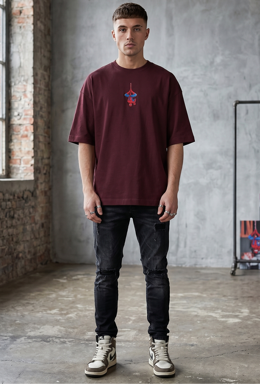Model wearing Small pixel-art Spider-Man hanging upside down in the center chest of a maroon oversized t-shirt