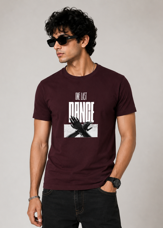 Male model wearing a maroon premium cotton graphic t-shirt featuring the "One Last Dance" typography with a monochrome artistic hand illustration on the front. Ideal for casual and streetwear fashion.
