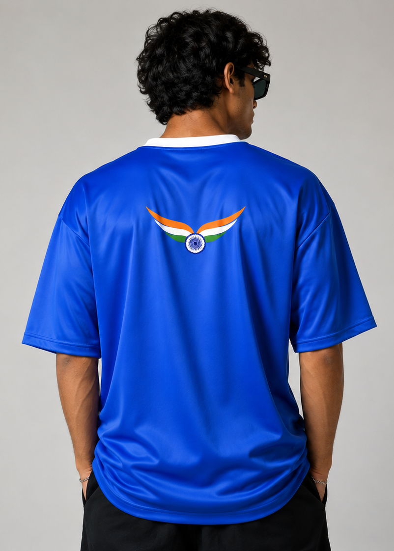 A man viewed from behind wearing a royal blue athletic t-shirt with a stylized winged logo on the back in orange, white, and blue. The background is a plain light gray studio backdrop.