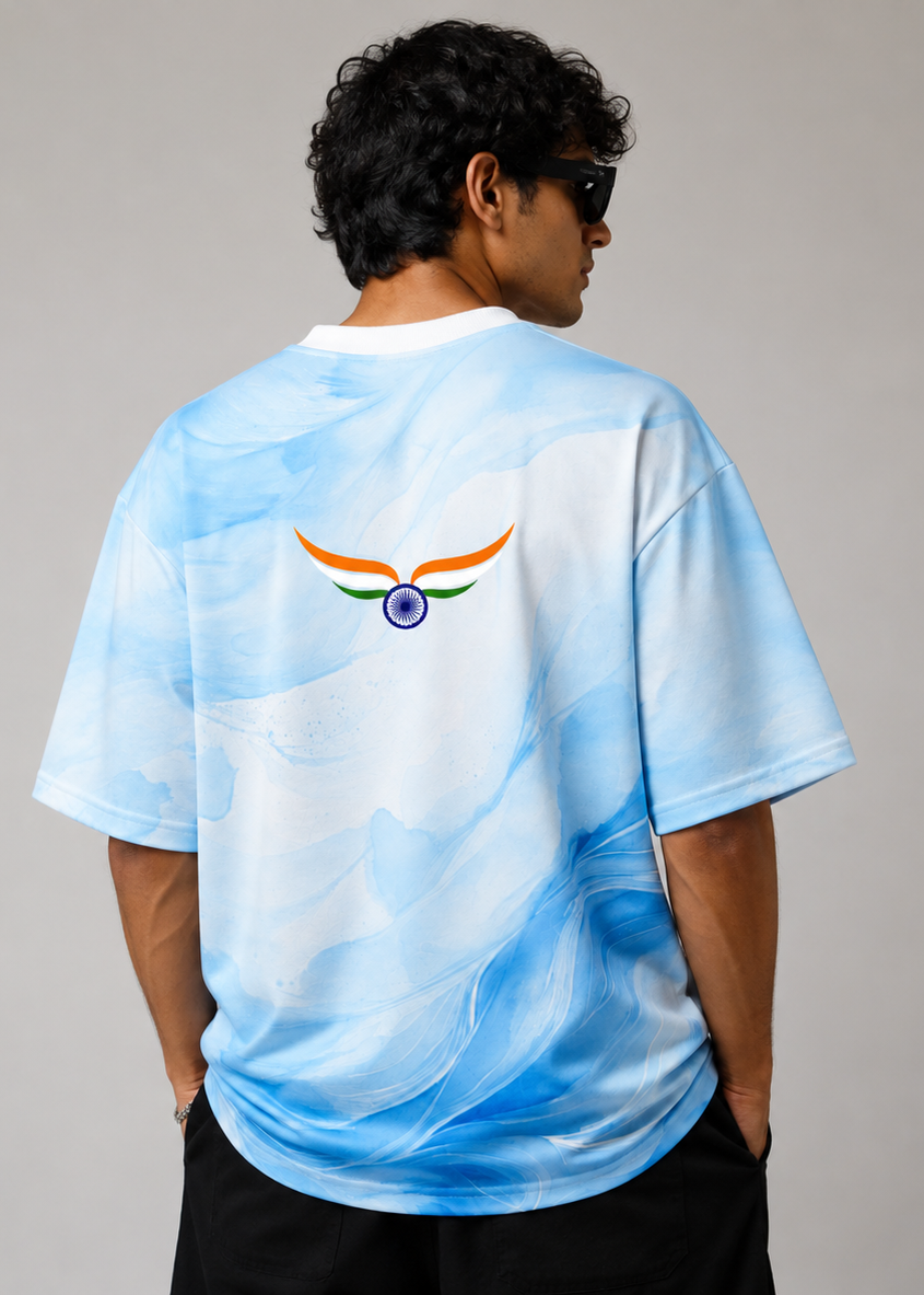 A man wearing a light blue and white marbled t-shirt from the back, featuring a stylized winged emblem with orange, green, and purple details. He is photographed against a neutral gray studio background.